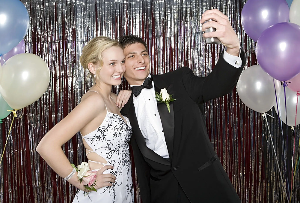 A young couple in formal attire taking a selfie at a party.