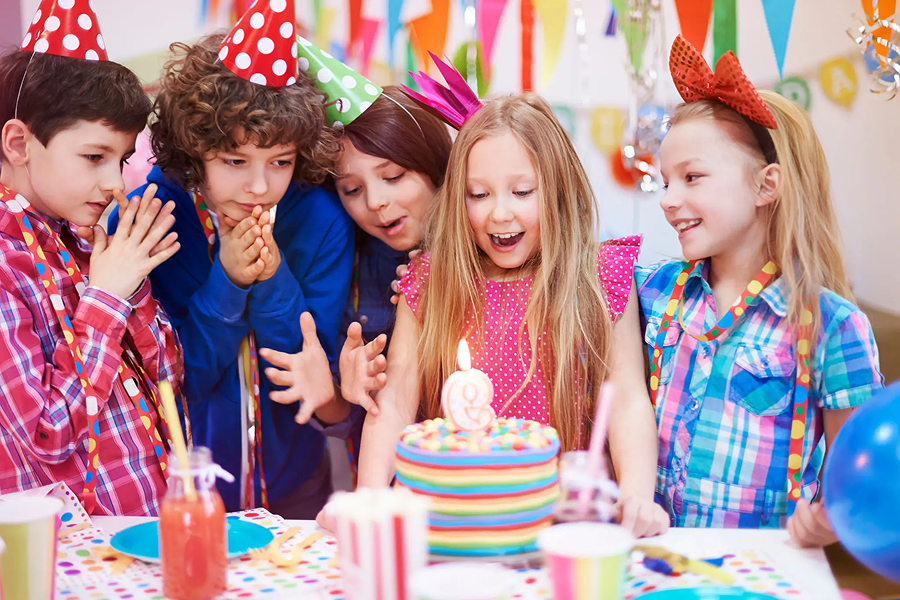 Kids celebrating a birthday with a colorful cake and party hats.