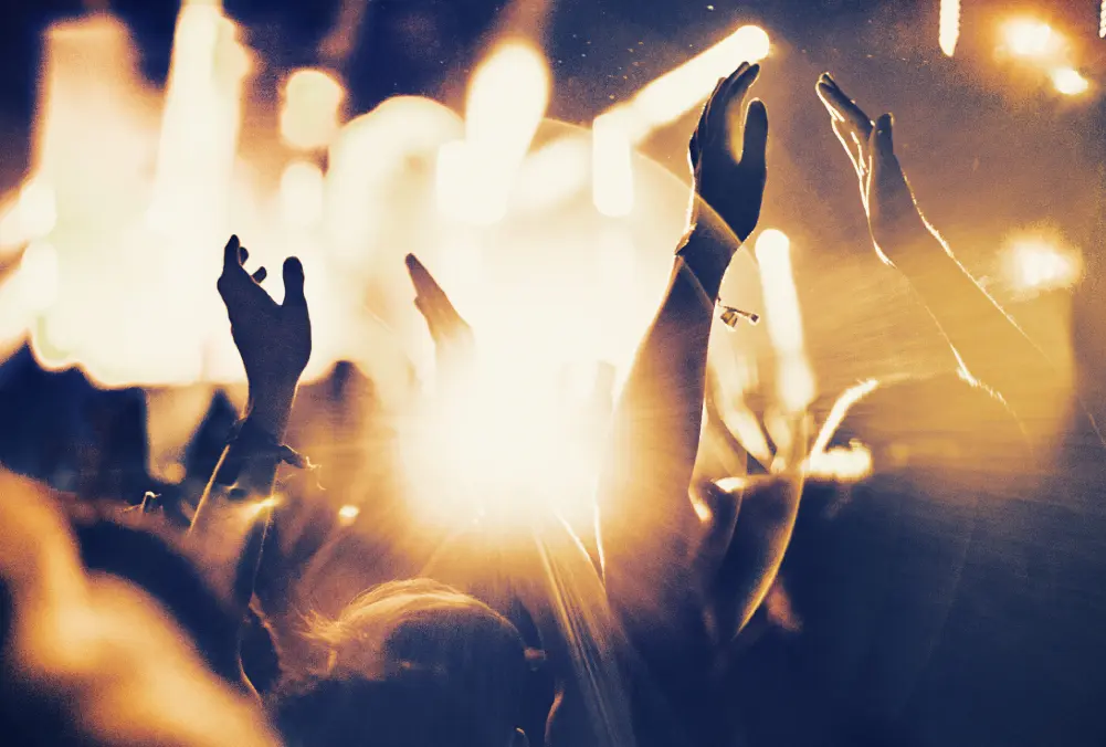 Hands raised in excitement at a vibrant concert with bright lights.