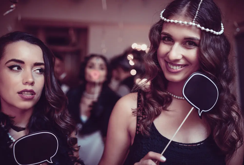 Two women smiling and holding props at a party.