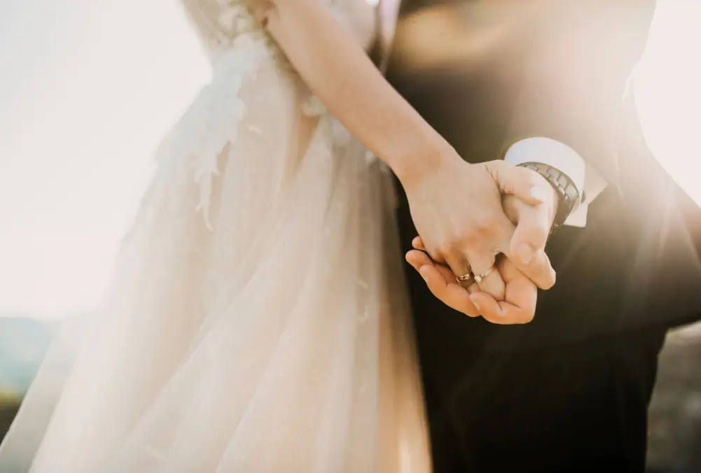 Couple holding hands gently, dressed in wedding attire.