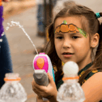 Young girl playing with a water gun at an outdoor event.